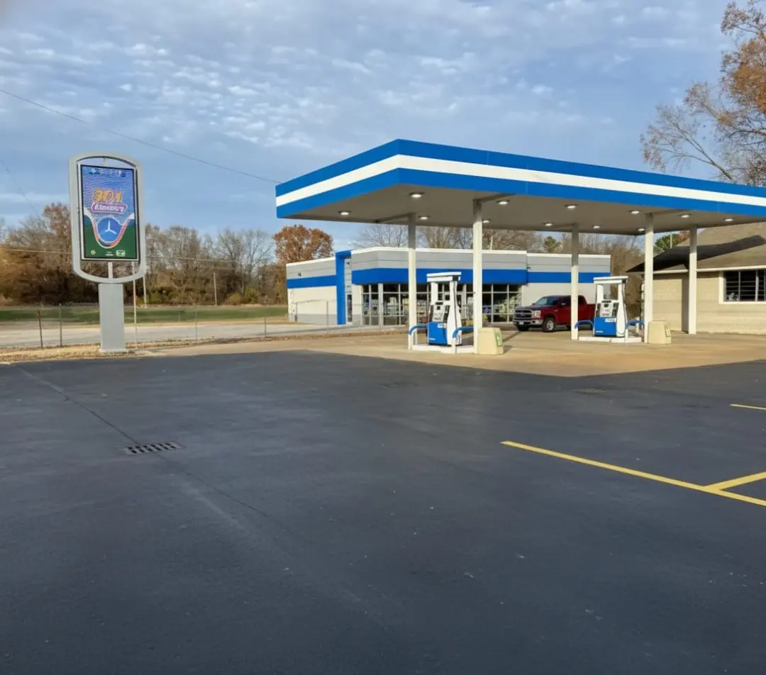 Blue and white gas station with fuel pumps and canopy in a large open parking area.